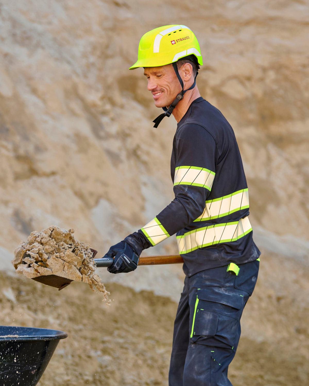 A bright yellow STRAUSS Baseball Style Hard Hat with a visor on a model digging sand on a construction site.