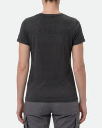 A woman wears the Women's STRAUSS Seamless Tee e.s.trail pure in black melange with work gloves and work pants, showing the shirt fit