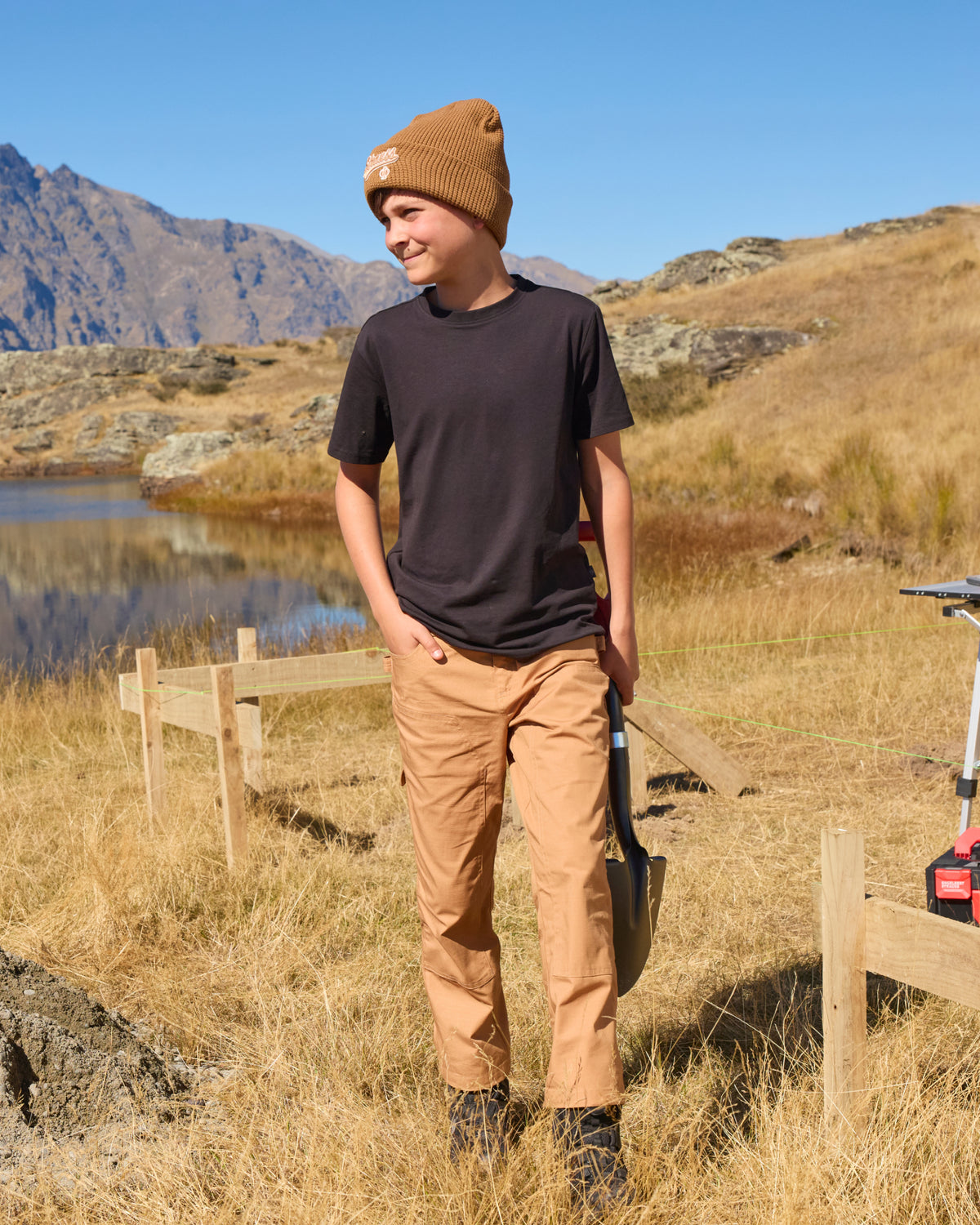A child wears the Kids' STRAUSS Cotton Stretch T-Shirt in black with kids' work pants while walking through a sunny field