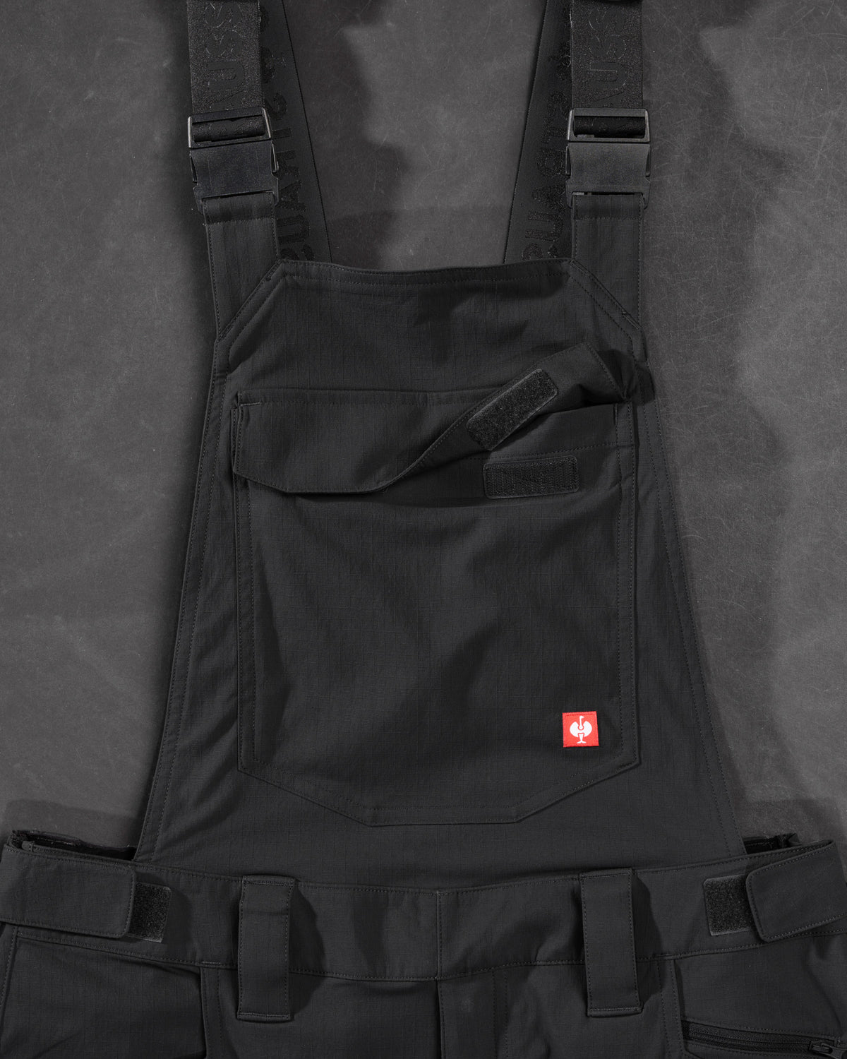 Close-up of black STRAUSS Stretch Ripstop Cargo Work Bib Overall e.s.taktik seam, hardware, and workwear details