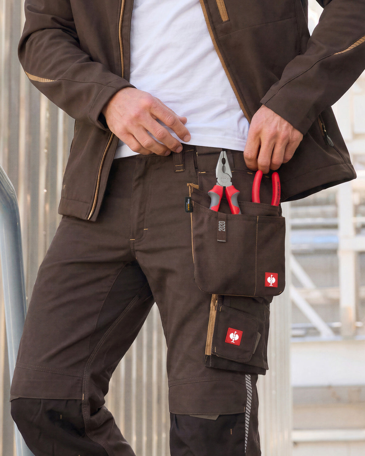 Large chestnut STRAUSS tool bag worn on matching work pants, with red-handled pliers in the pockets.