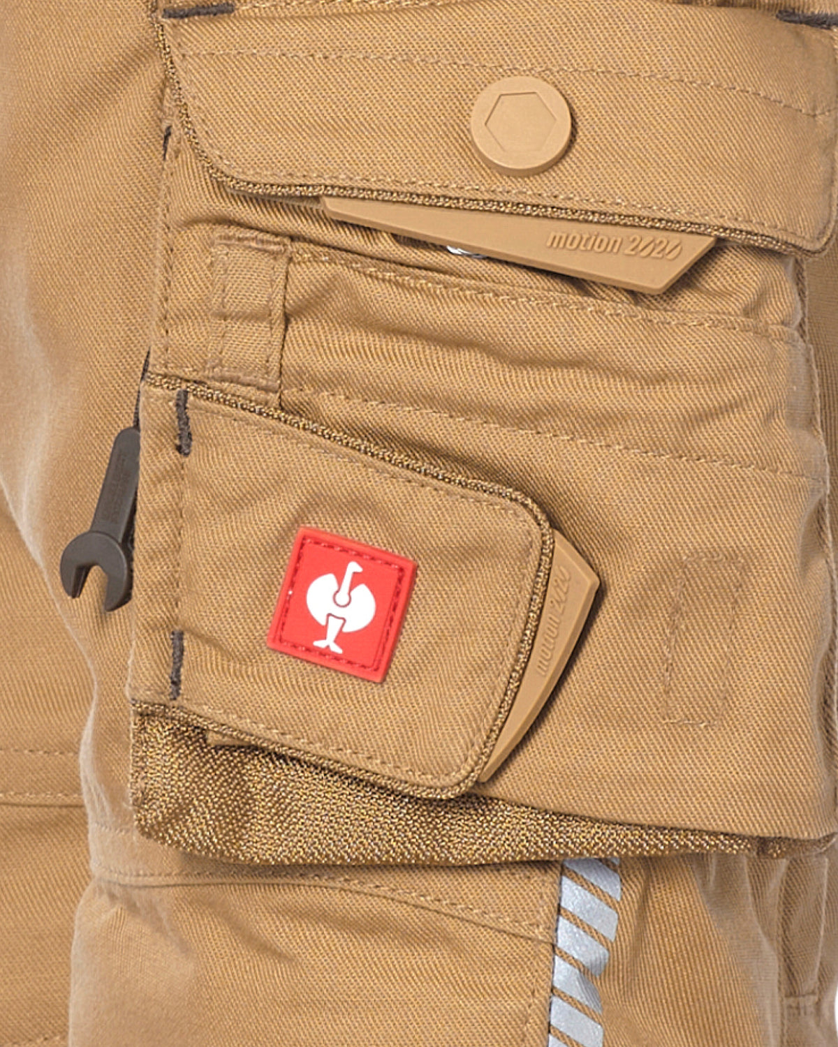 Close-up of tan canvas cargo pants showing a front utility pocket with a red STRAUSS patch featuring a white rooster logo, a snap-tab flap, and a small black hook tool tucked into the pocket.