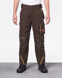 A person wearing dark brown work pants with multiple utility pockets, contrast tan stitching, and black work boots, shown from the waist down against a light gray studio background.
