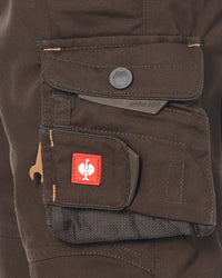 Close-up of a dark brown shorts cargo pocket with a red square patch featuring a white rooster logo, a gray snap button, and a gray metal tool clip.