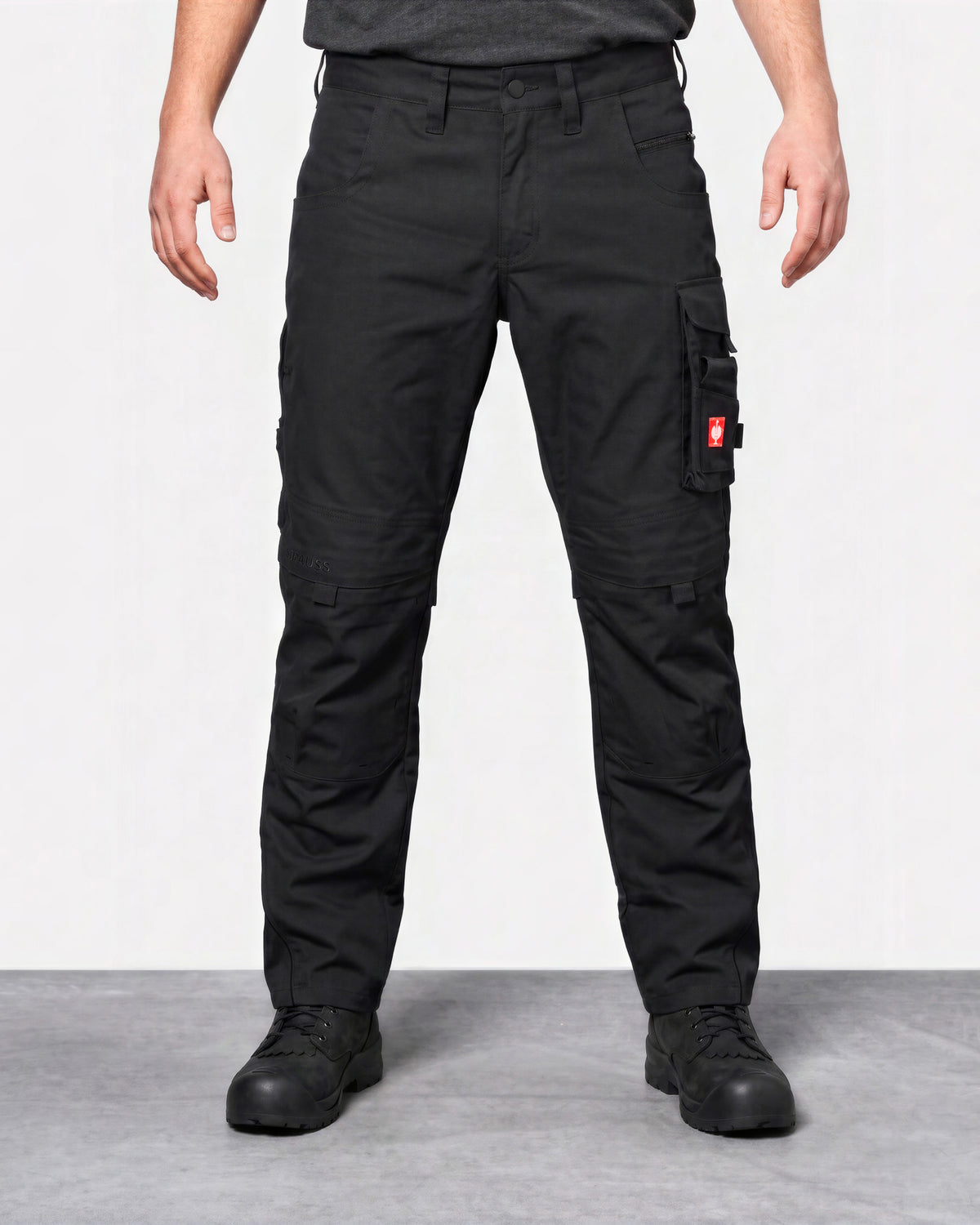 A person wearing black cargo pants with multiple utility pockets and black work boots, standing against a light gray studio background.
