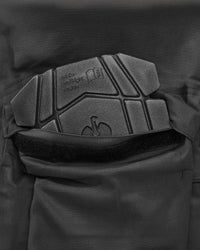 Close-up of a black tactical vest or jacket showing a padded chest protector with embossed branding and a hook-and-loop closure.