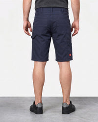 A man viewed from the back wearing navy blue cargo shorts, a dark gray t-shirt, and black sneakers, standing against a light gray studio background.