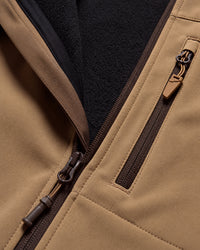 Close-up of a tan fleece-lined zippered jacket showing the tan exterior fabric, dark brown zipper trim, and a black fleece interior.