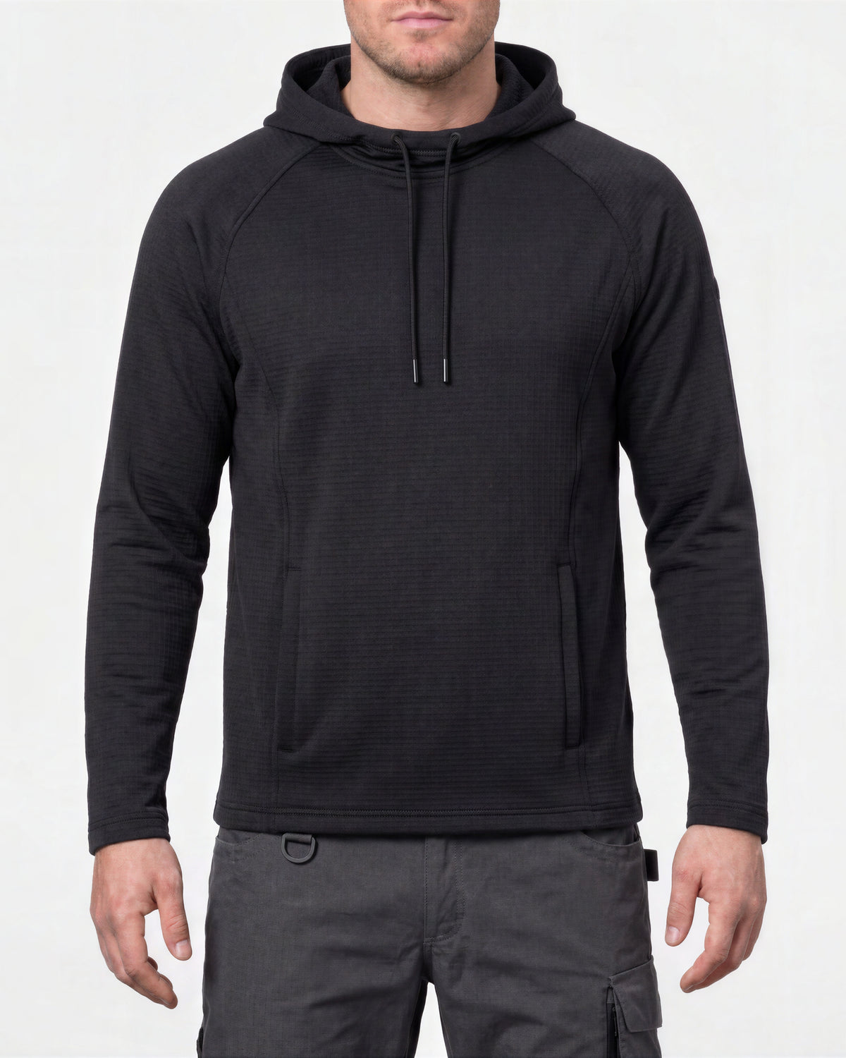 A man wearing a black long-sleeve hooded pullover with a textured knit fabric, drawstrings, and a front kangaroo pocket, paired with dark gray cargo pants, against a plain white background.
