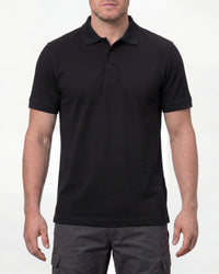 A model wears the STRAUSS Cotton Polo Shirt in black with tan work pants and work boots in a studio product scene