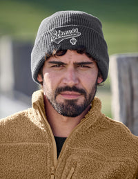 Man wearing a beanie with a logo and a jacket outdoors