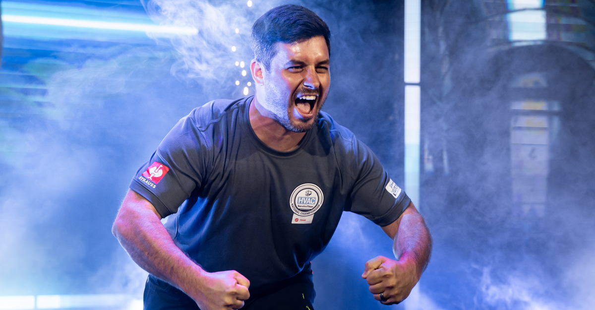 A man in a sports shirt clenches his fists and yells passionately, surrounded by dramatic smoke and colorful lighting on stage.