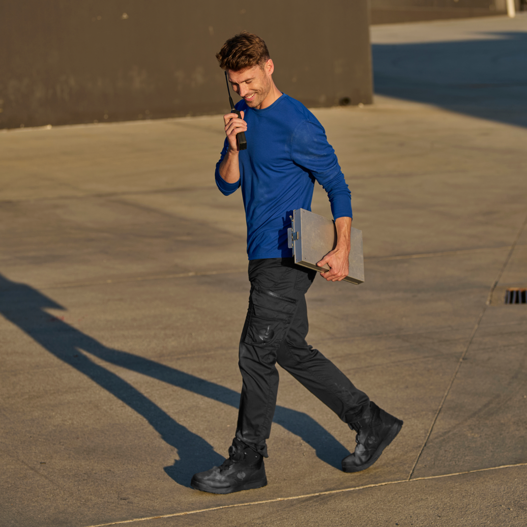 A man wearing a blue shirt and black pants talking into a walkie talkie