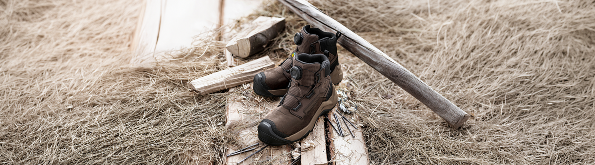 A pair of brown STRAUSS safety toe work shoes onto some wood and hay