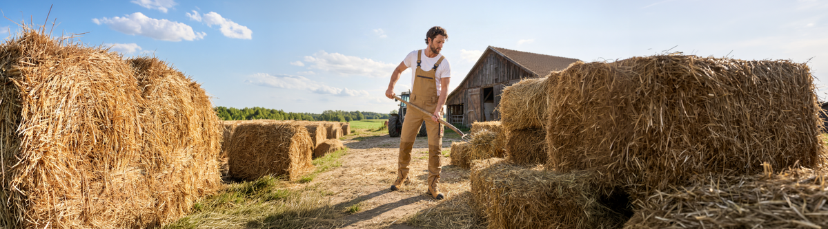 A man working with a pitchfork moving hay infront of a barn