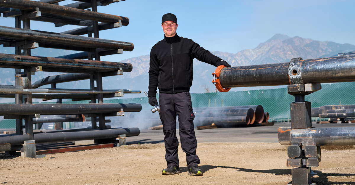 A man wearing black workwear standing next to some metal pipes on a pipe storage.
