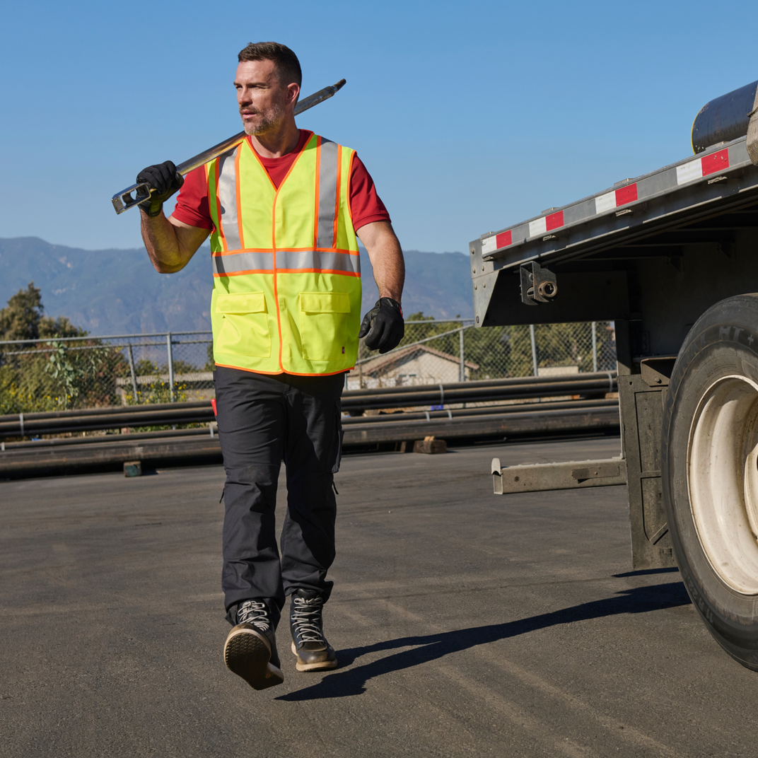 Man in a yellow safety vest walking on a road with a truck in the background