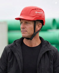 A bright red STRAUSS Baseball Style Hard Hat with a visor on a model as seen from the front 3/4 angle. 