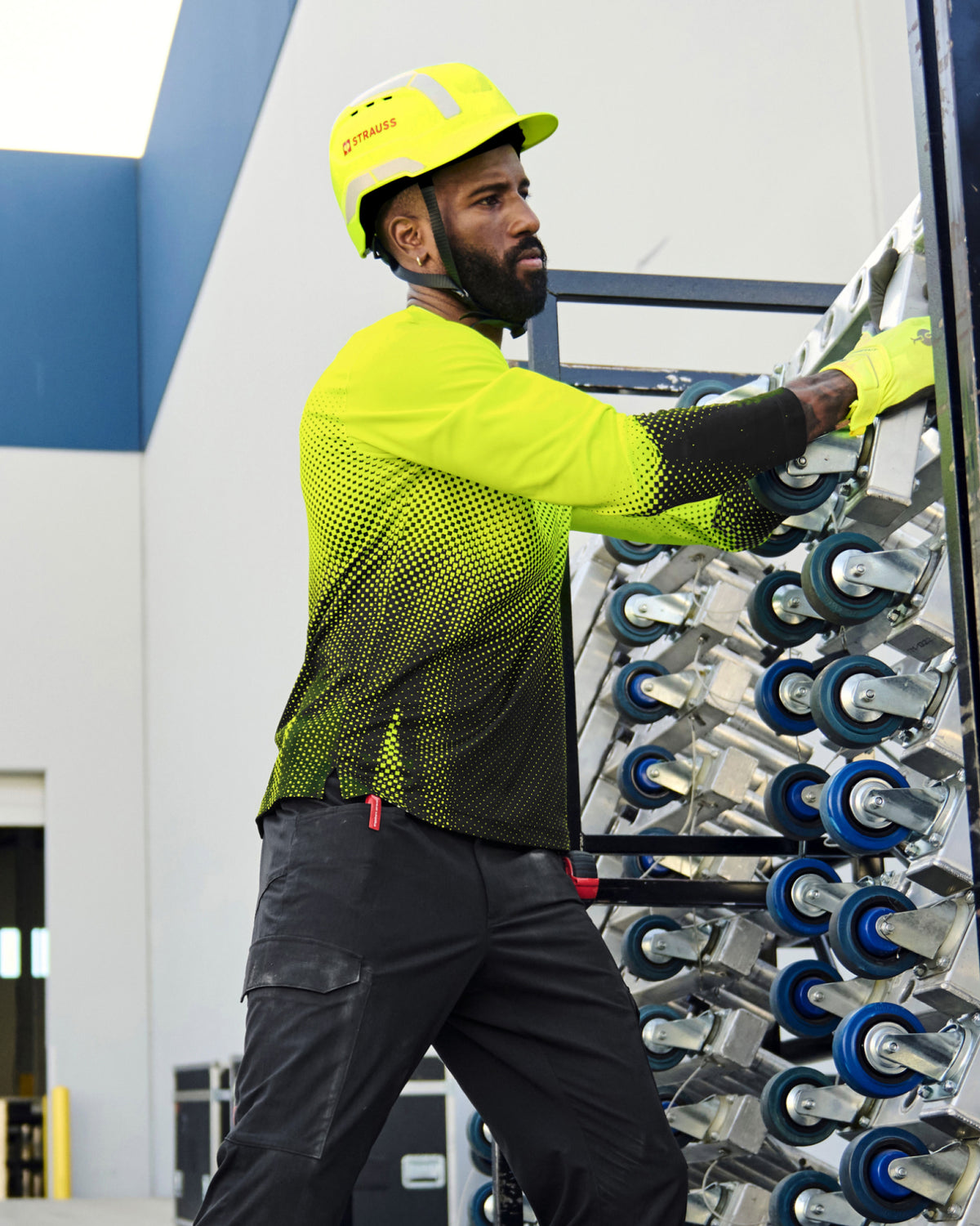 A bright yellow STRAUSS Baseball Style Hard Hat with a visor on a model working in a wheel factory.
