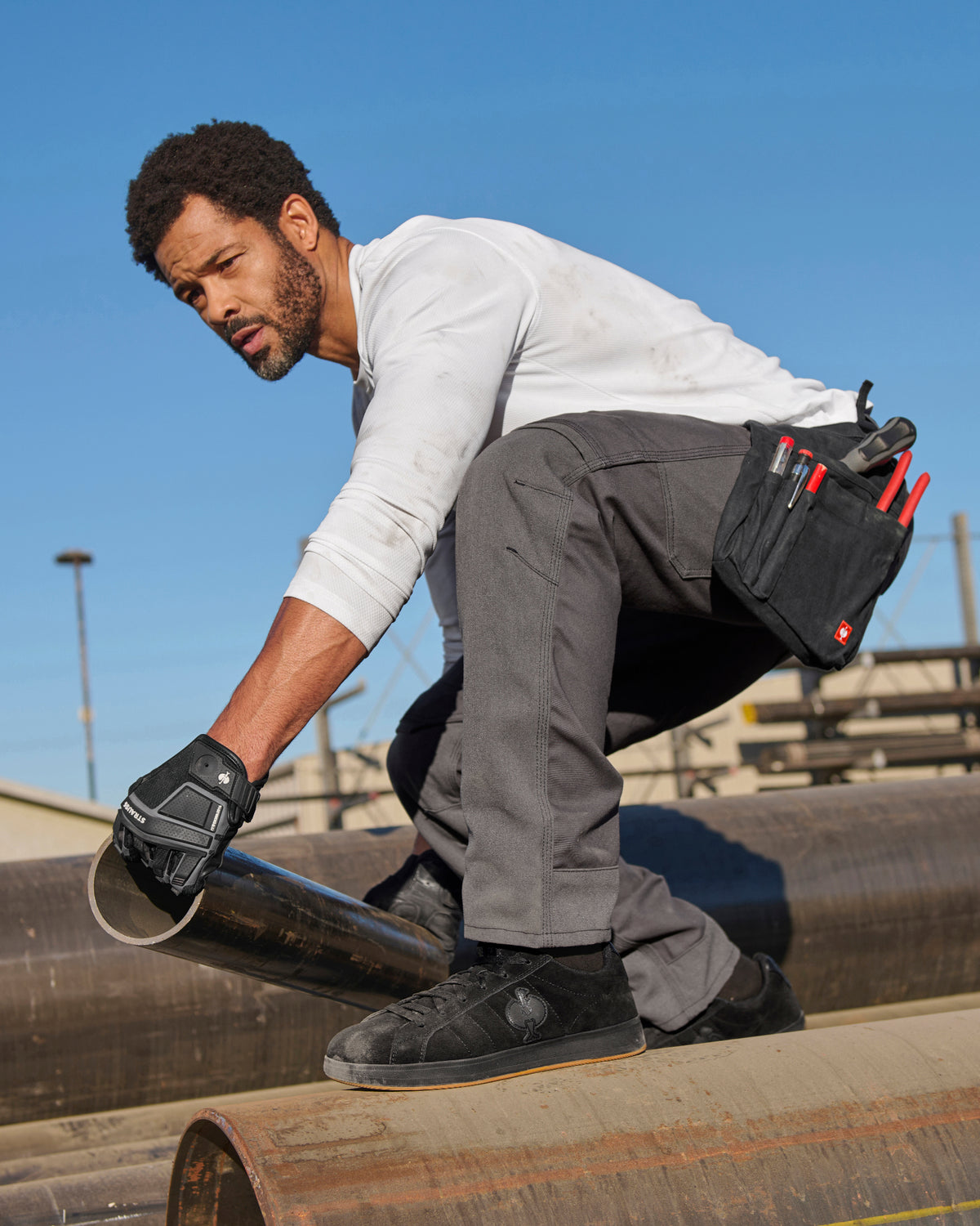 A worker wears the STRAUSS Performance Long Sleeve Shirt in white with tan work pants beside jobsite equipment