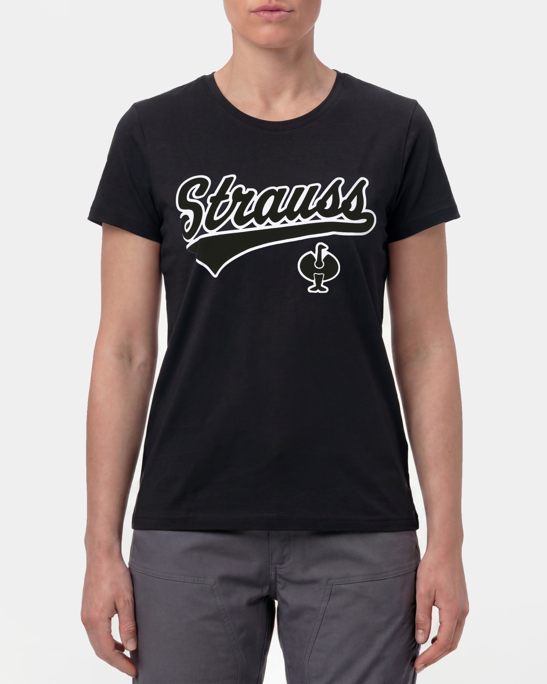 A woman wears the Women's STRAUSS Artwork T-Shirt e.s.e:pic in black with work pants and work boots in a studio product scene