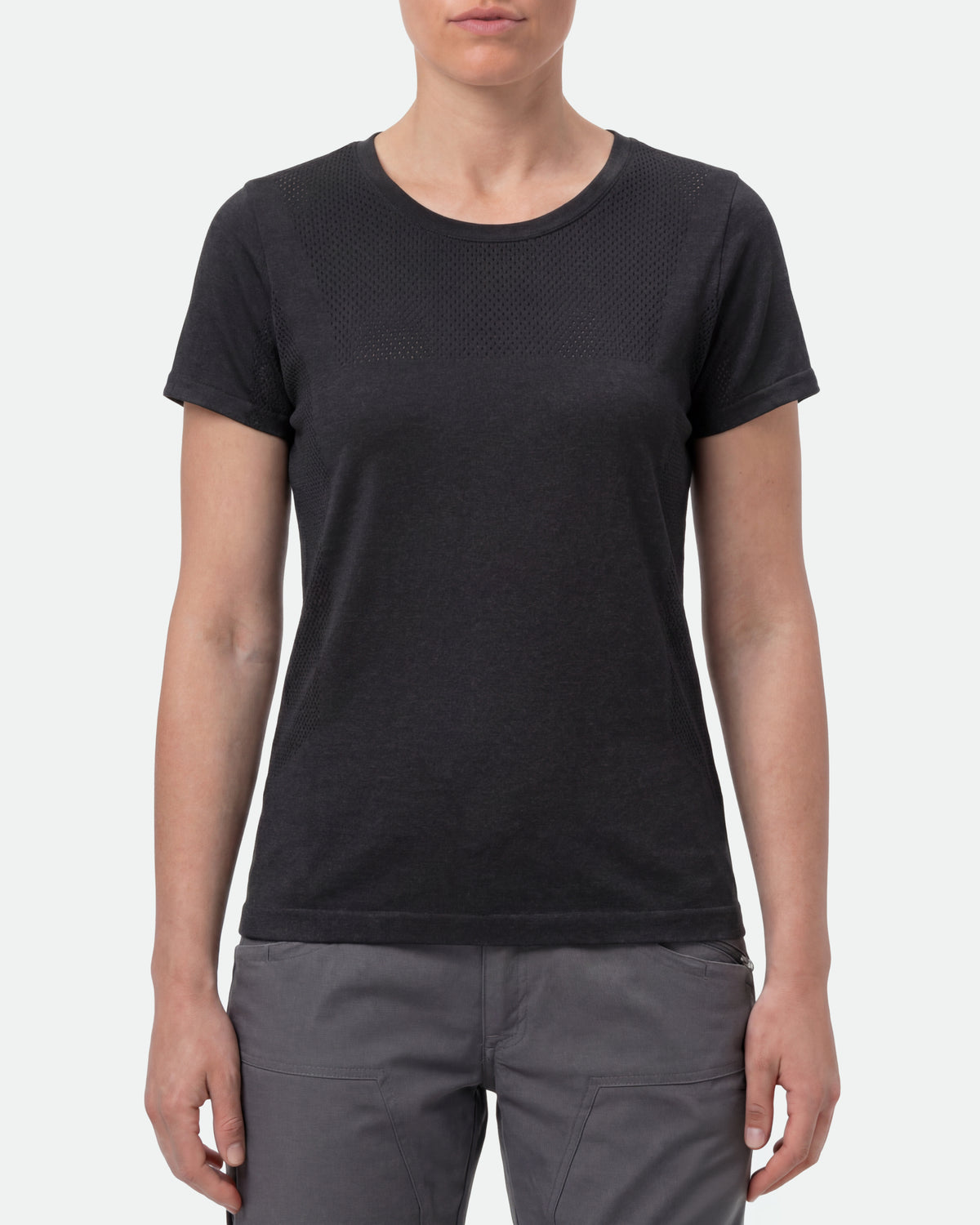 A woman wears the Women's STRAUSS Seamless Tee e.s.trail pure in black melange with work gloves and work pants in a studio product scene