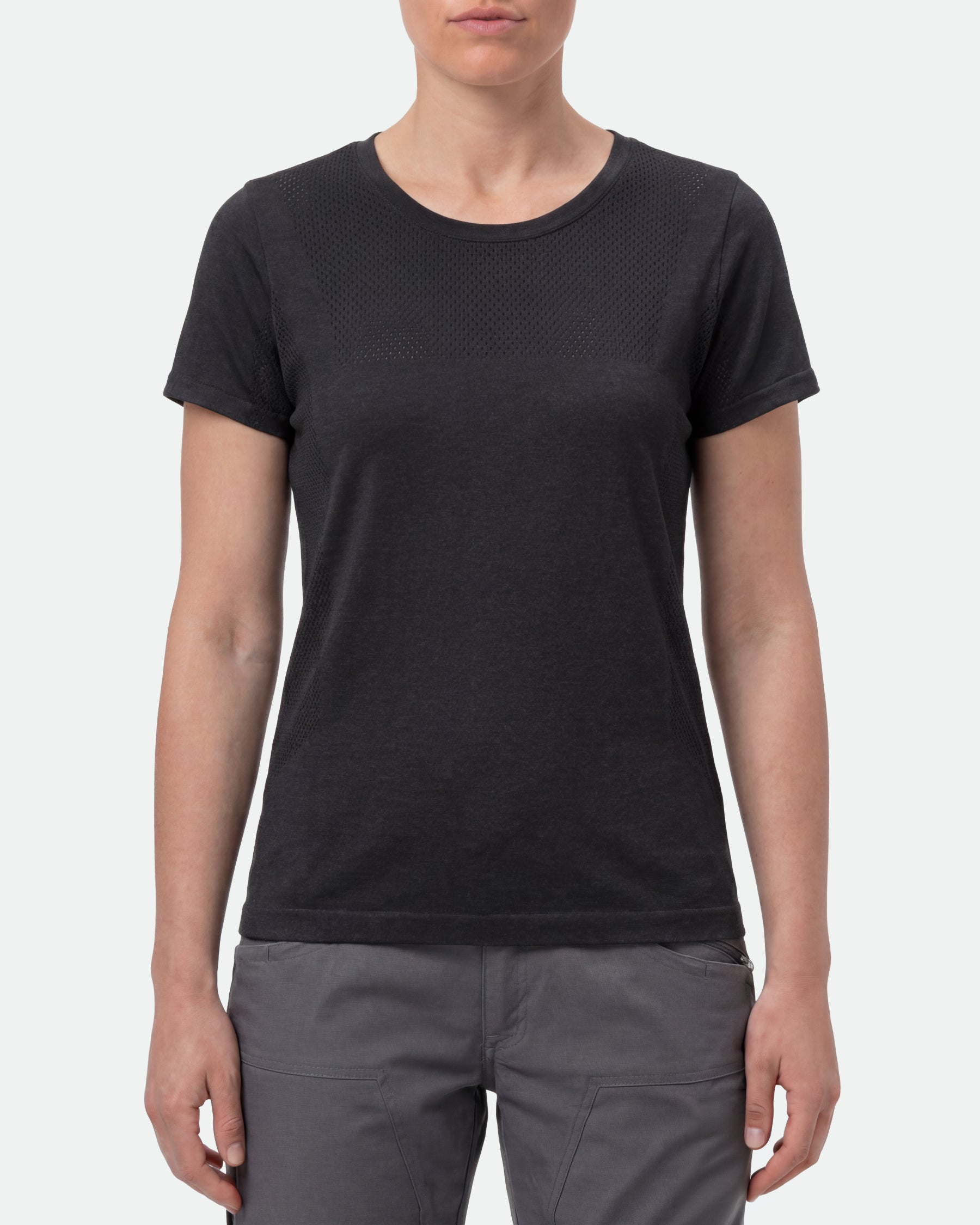 A woman wears the Women's STRAUSS Seamless Tee e.s.trail pure in black melange with work gloves and work pants in a studio product scene