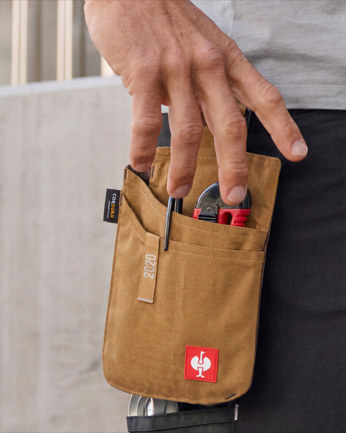 Hand reaching into a small almond brown STRAUSS tool bag holding pliers at the hip.