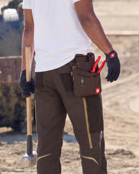 Worker carrying a sledgehammer wears a medium chestnut STRAUSS tool bag with red-handled tools at the hip.
