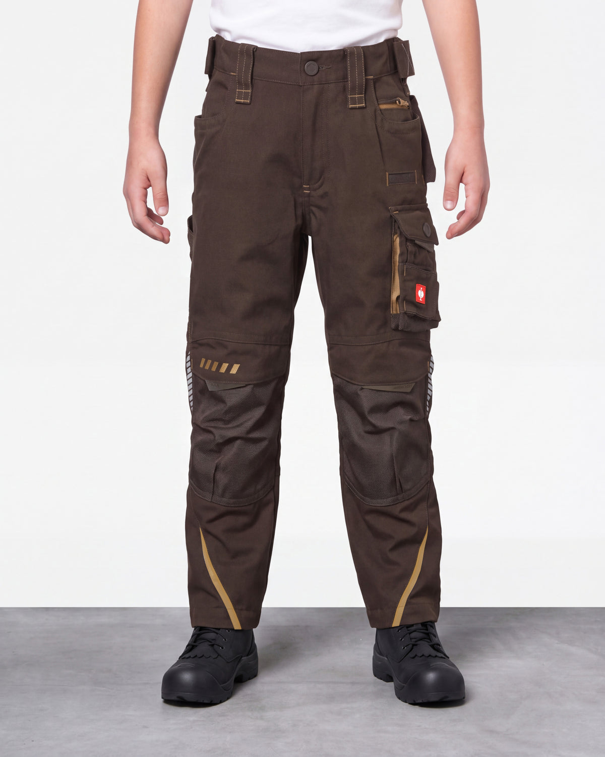 A person wearing dark brown work pants with multiple utility pockets, contrast tan stitching, and black work boots, shown from the waist down against a light gray studio background.