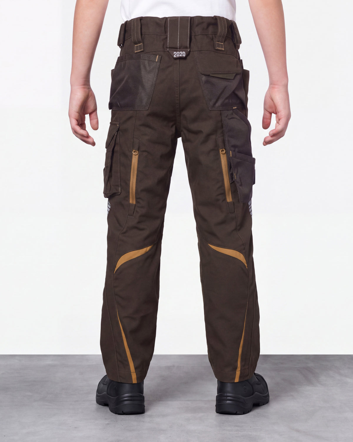 A person shown from the back wearing dark brown cargo work pants with tan contrast panels and black shoes, standing against a plain light gray studio background.