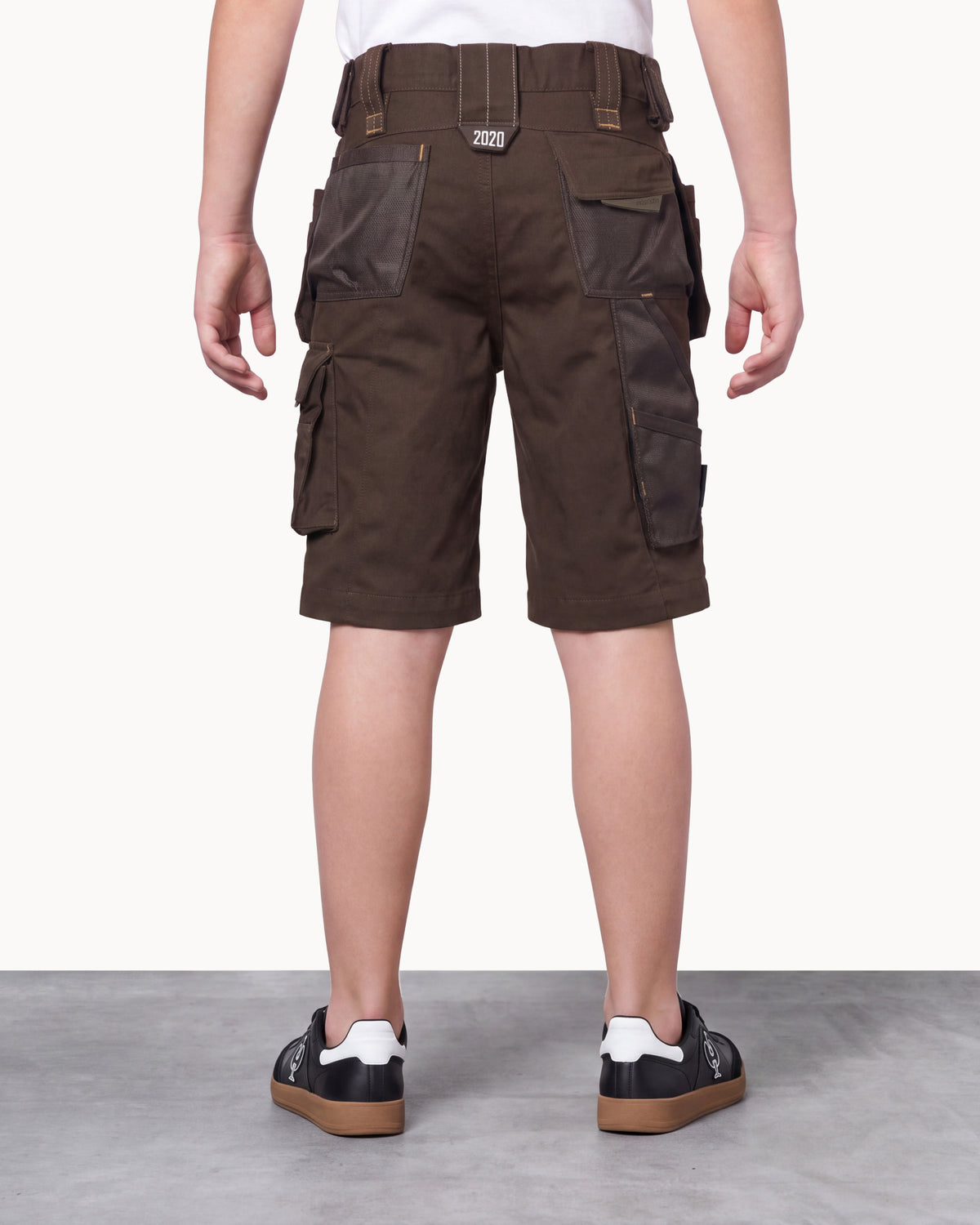 A person shown from the back wearing dark brown cargo shorts with multiple flap pockets and a matching belt, paired with black sneakers, against a plain light studio background.
