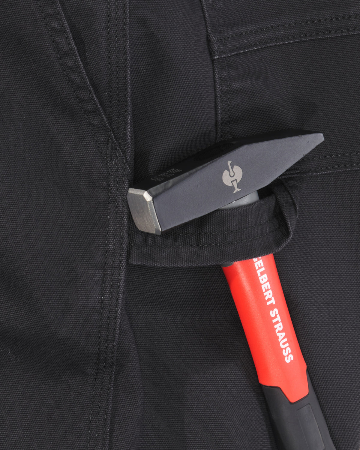 Close-up of a black tool pouch on dark workwear pants, holding a red and black hand tool with a silver metal head. The brand name 'ENGELBERT STAUSS' is visible on the tool handle.