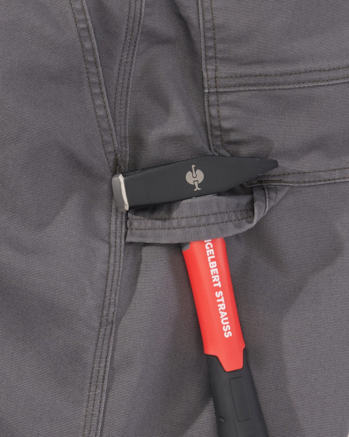 A close-up of a gray fabric pocket holding a black pocket knife with a silver blade, next to a red and black Iceberg Strauss tool with white branding.