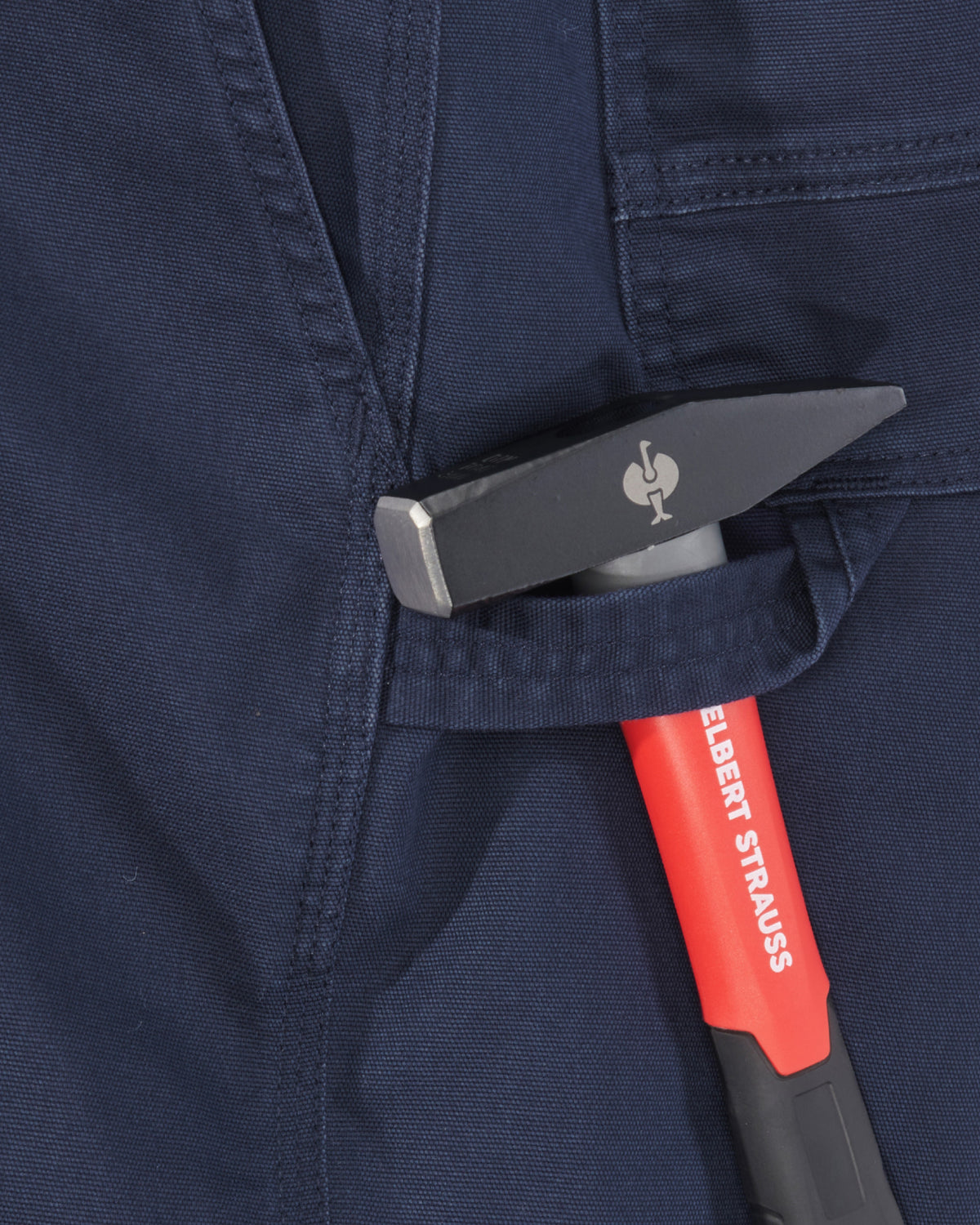 Close-up of a dark navy workwear fabric pocket holding a hammer with a red and black handle and a silver metal head.