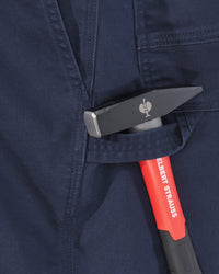 Close-up of a dark navy workwear fabric pocket holding a hammer with a red and black handle and a silver metal head.