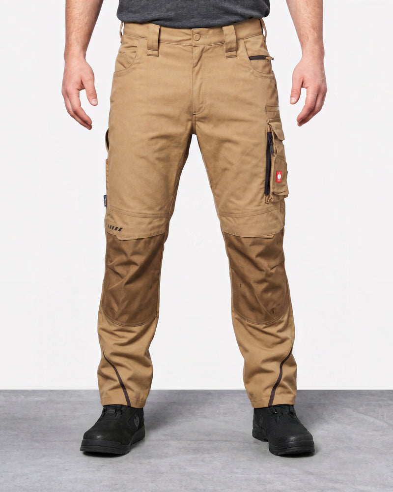 A person wearing tan cargo work pants with darker brown reinforced knee panels and black work boots, shown from the waist down against a light gray studio background.