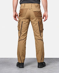 A person shown from the back wearing tan cargo work pants with black zippers and black shoes, photographed against a light gray studio background.