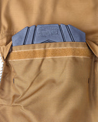 Close-up detail of a tan technical knee pad pocket showing a knee pad and a tan hook-and-loop strap.