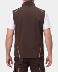 A man viewed from the back wearing a brown sleeveless zip vest over a white t-shirt and dark cargo pants, against a light gray studio background.
