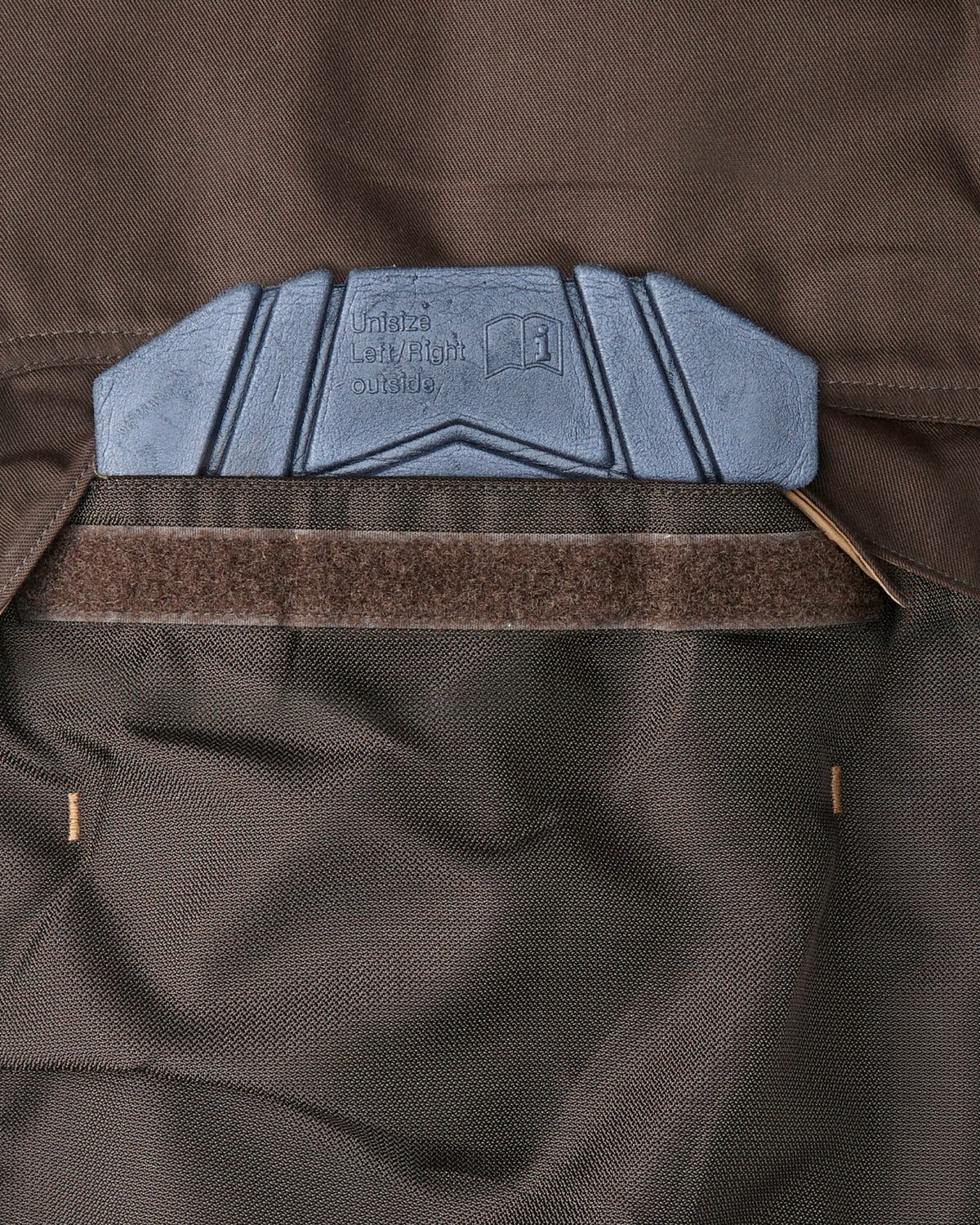 Close-up of a brown bib pocket showing a blue-gray molded knee pad.