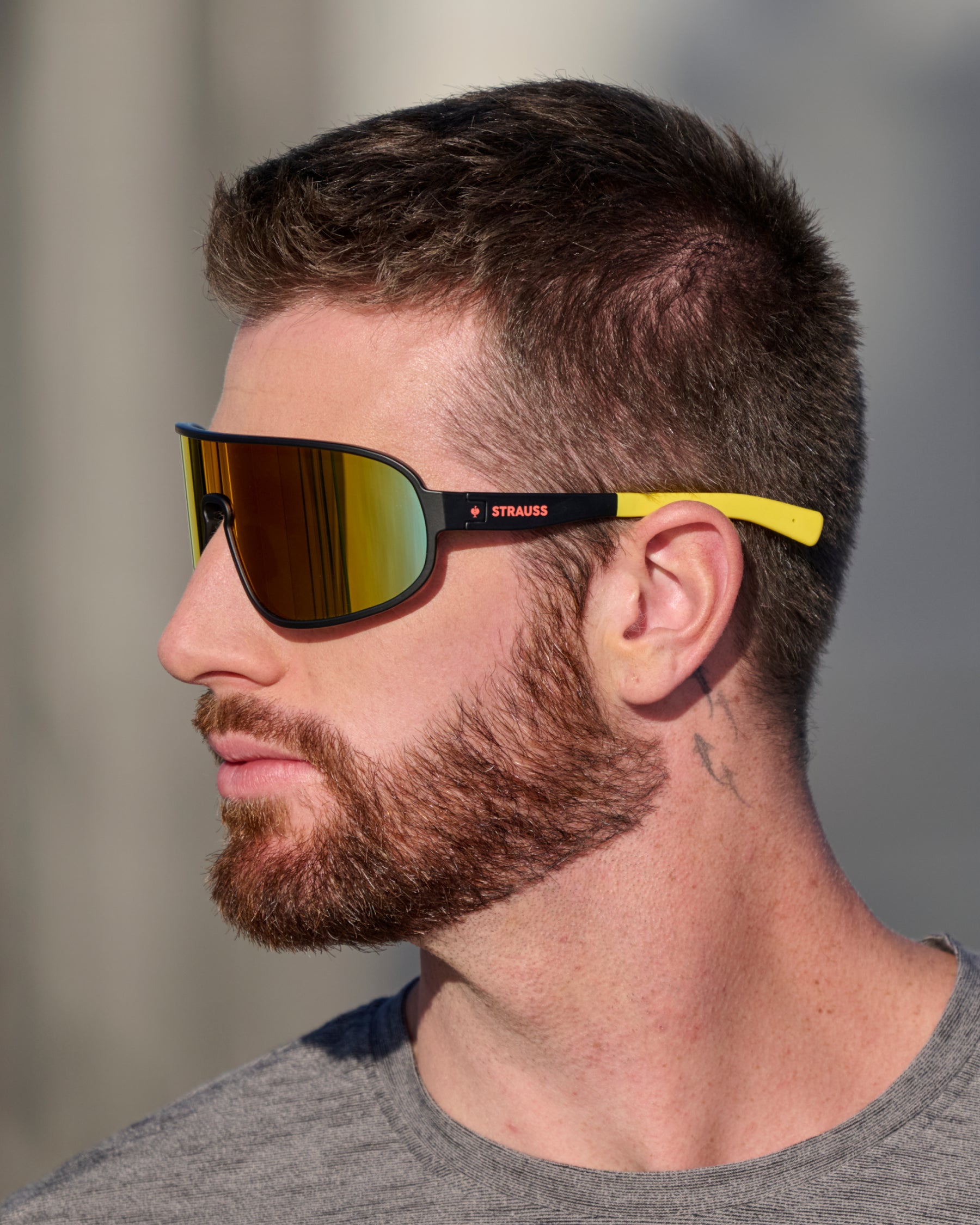 A close lifestyle scene shows black and high-vis yellow STRAUSS e.s.ambition race sunglasses worn with a work shirt outdoors.