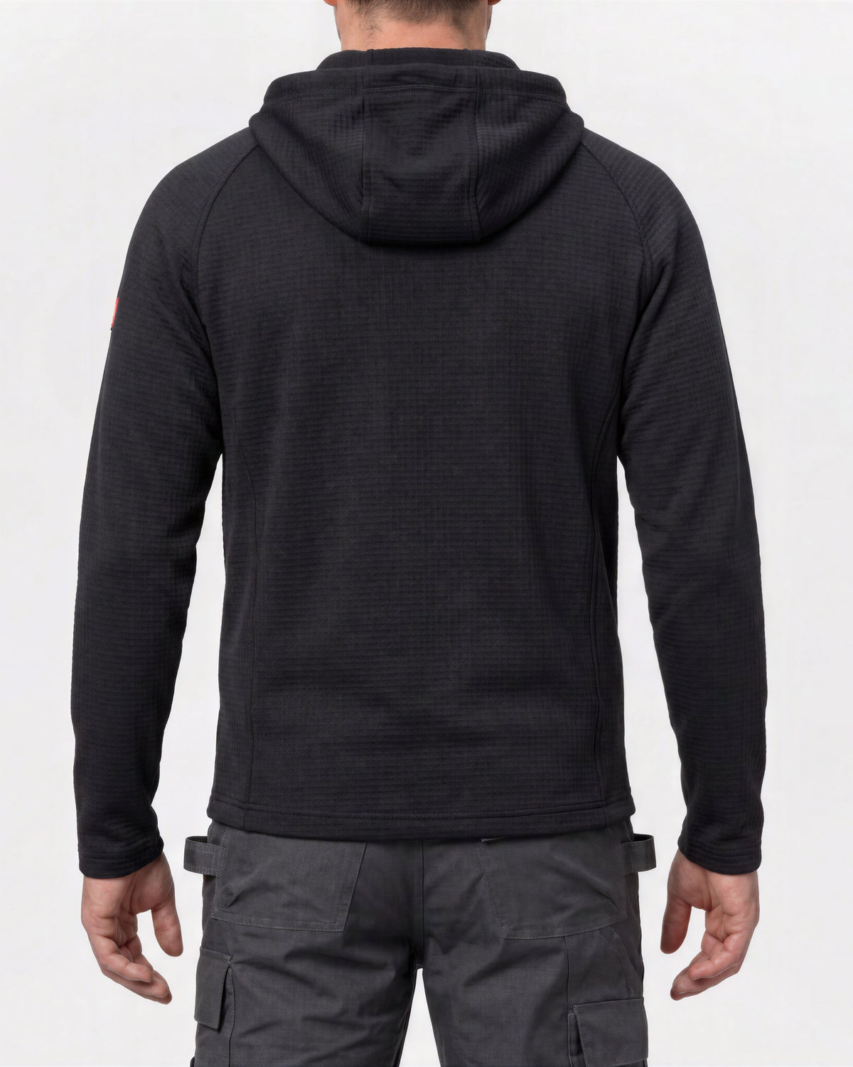 A man viewed from the back wearing a black textured hooded sweatshirt and dark gray cargo pants against a plain white studio background.