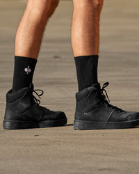 A person wears black STRAUSS classic all-round high-cut socks, 3-pack with work shoes in a casual product scene.