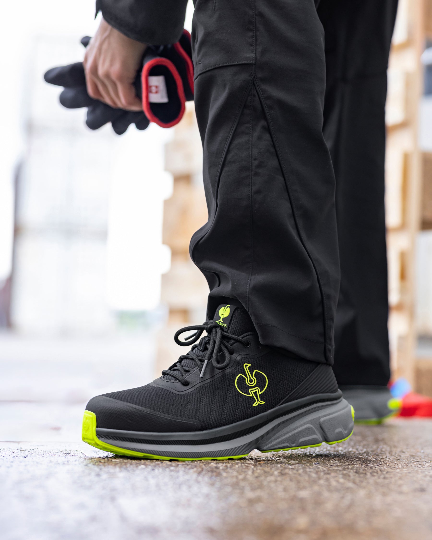 A close-up of a person's leg wearing a black athletic sneaker with a bright neon yellow-green logo and sole accent, standing on a wet concrete surface.