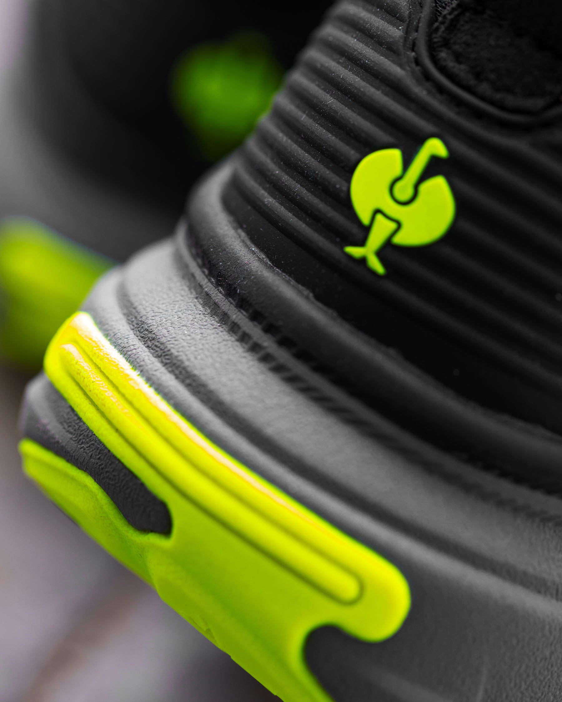 Close-up of a black athletic shoe with bright neon yellow-green accents, including a matching logo on the heel collar and a chunky sole.