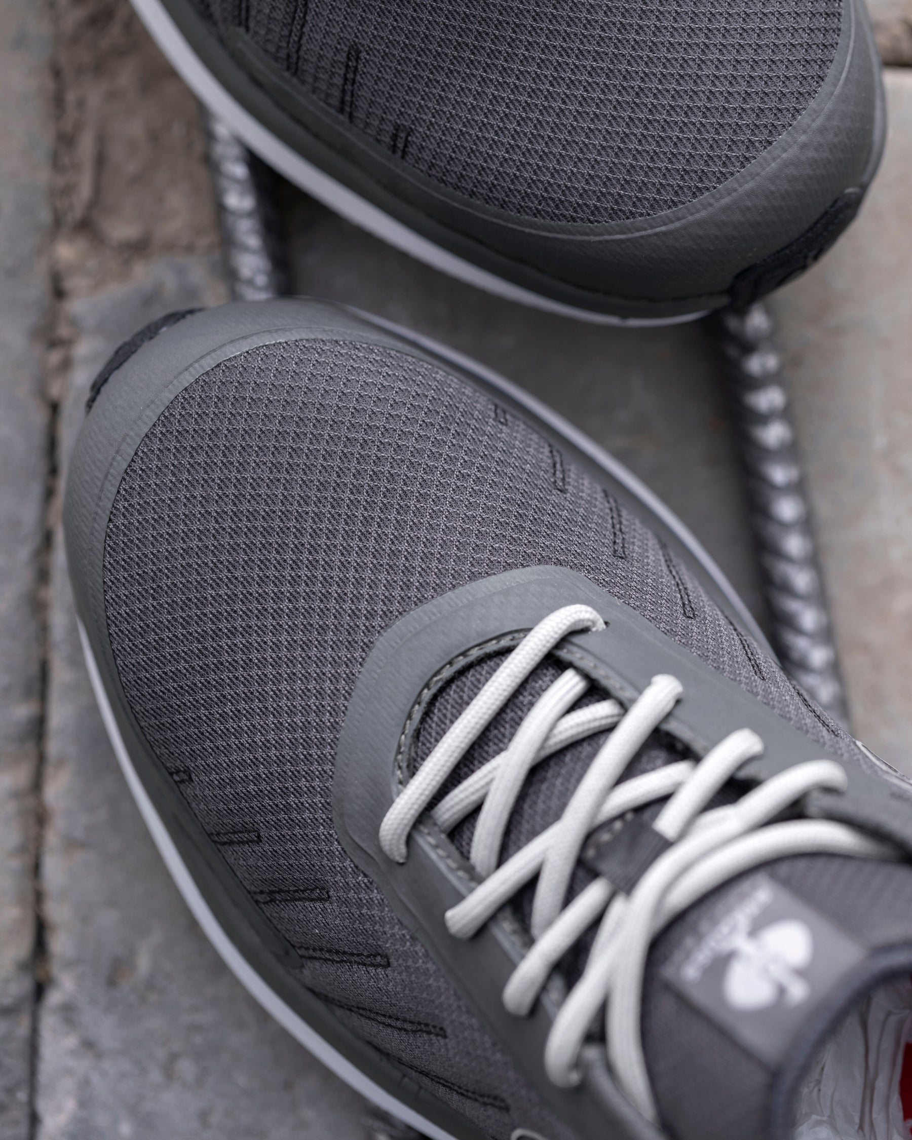 Close-up of a gray mesh athletic sneaker with white laces, resting on a stone surface next to a coiled metal cable.