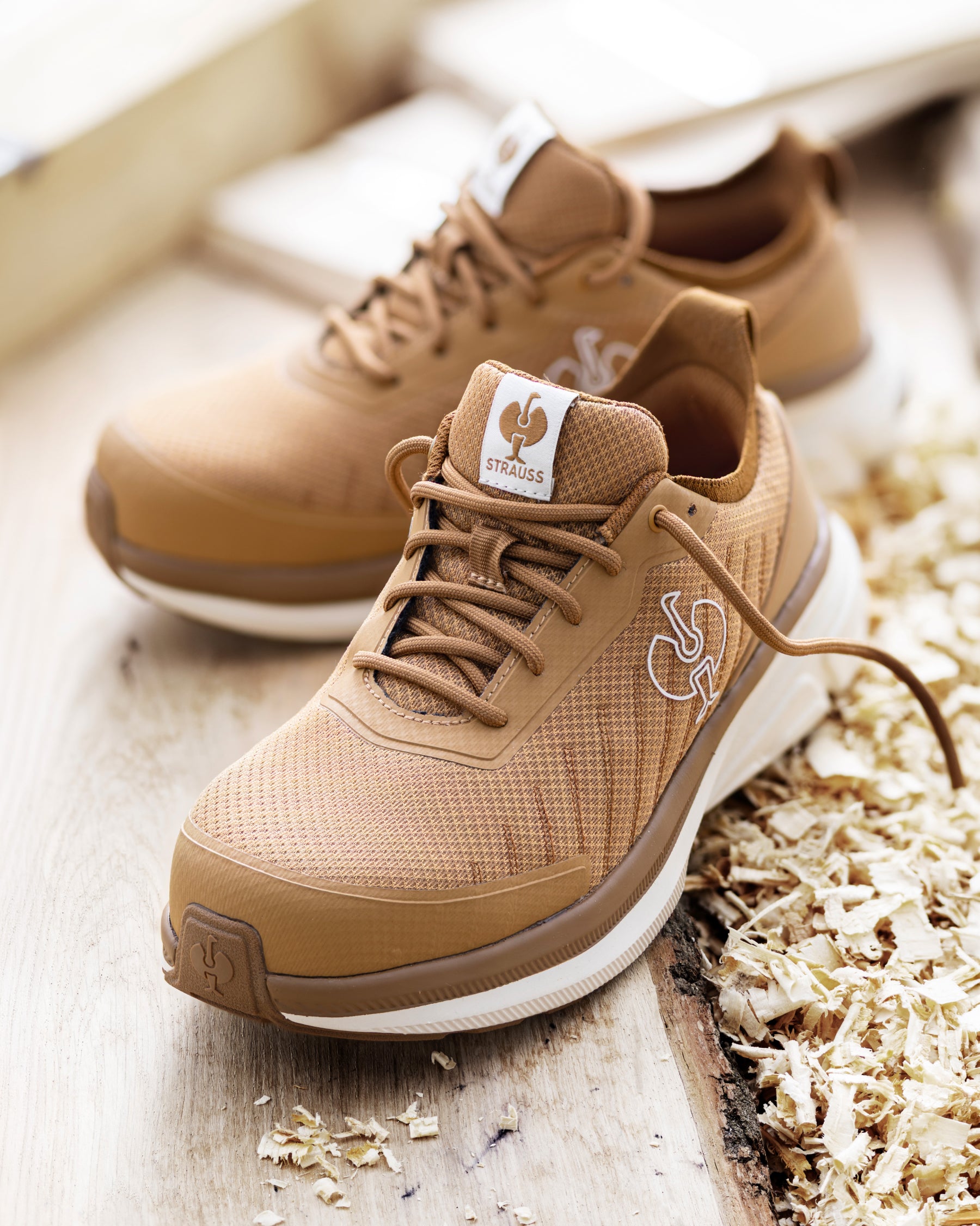 A pair of tan and brown mesh sneakers with white soles, styled on a light wooden surface next to wood shavings. The brand logo on the tongue patch reads 'SOLSBERG'.