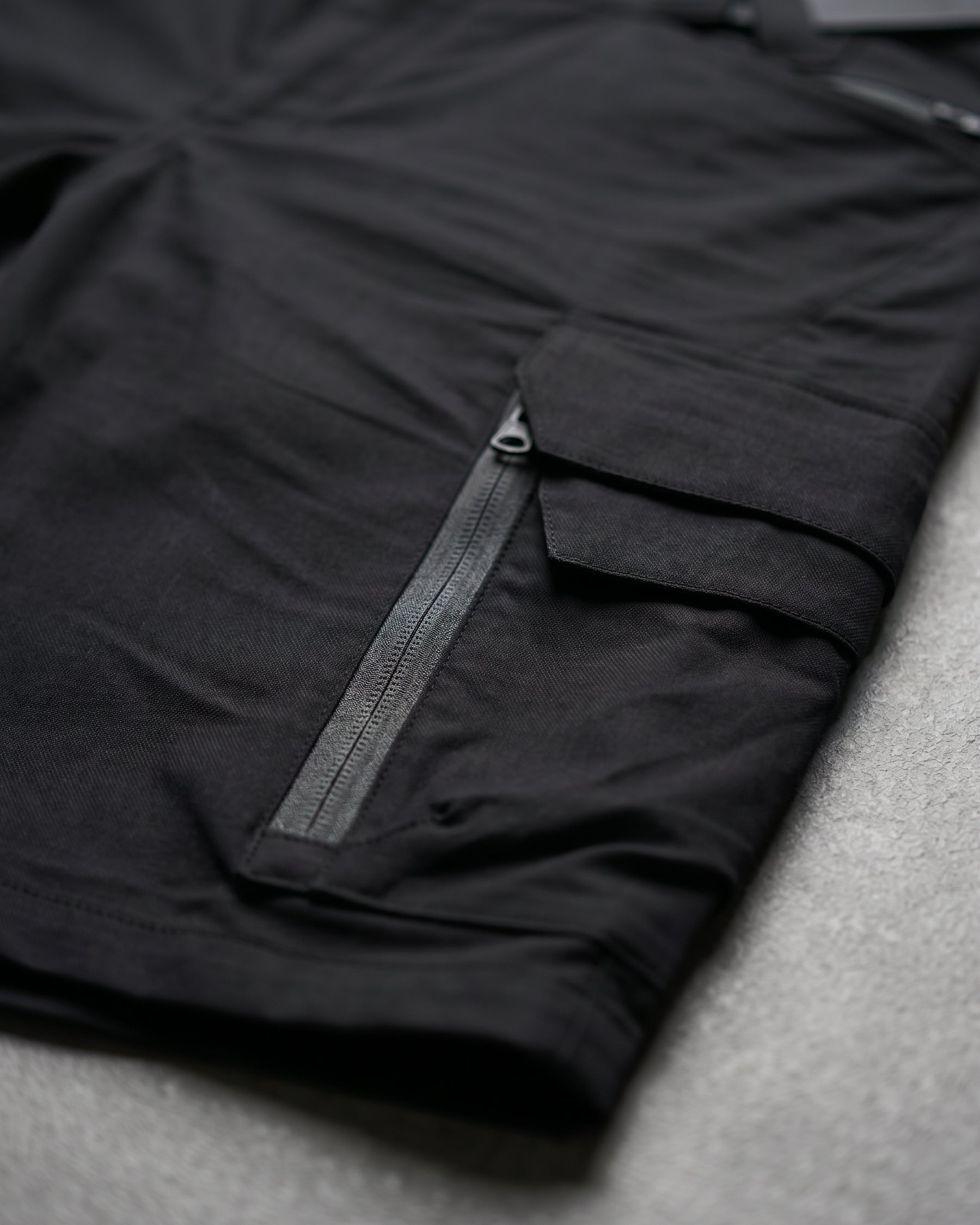 Close-up detail of Engelbert Strauss women's e.s. trail pure cargo work shorts in black and carbon gray, focusing on the utility pocket area, seams, and reinforced workwear construction.