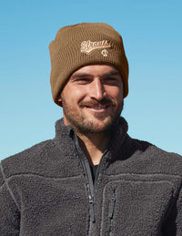 Man wearing a brown knit beanie with branding against a clear blue sky